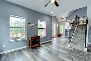 A spacious room with hardwood flooring, a ceiling fan, and a staircase leading to another level.