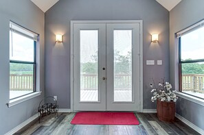 A room with a double door, two wall-mounted lights, a red doormat, and a wooden barrel with flowers.