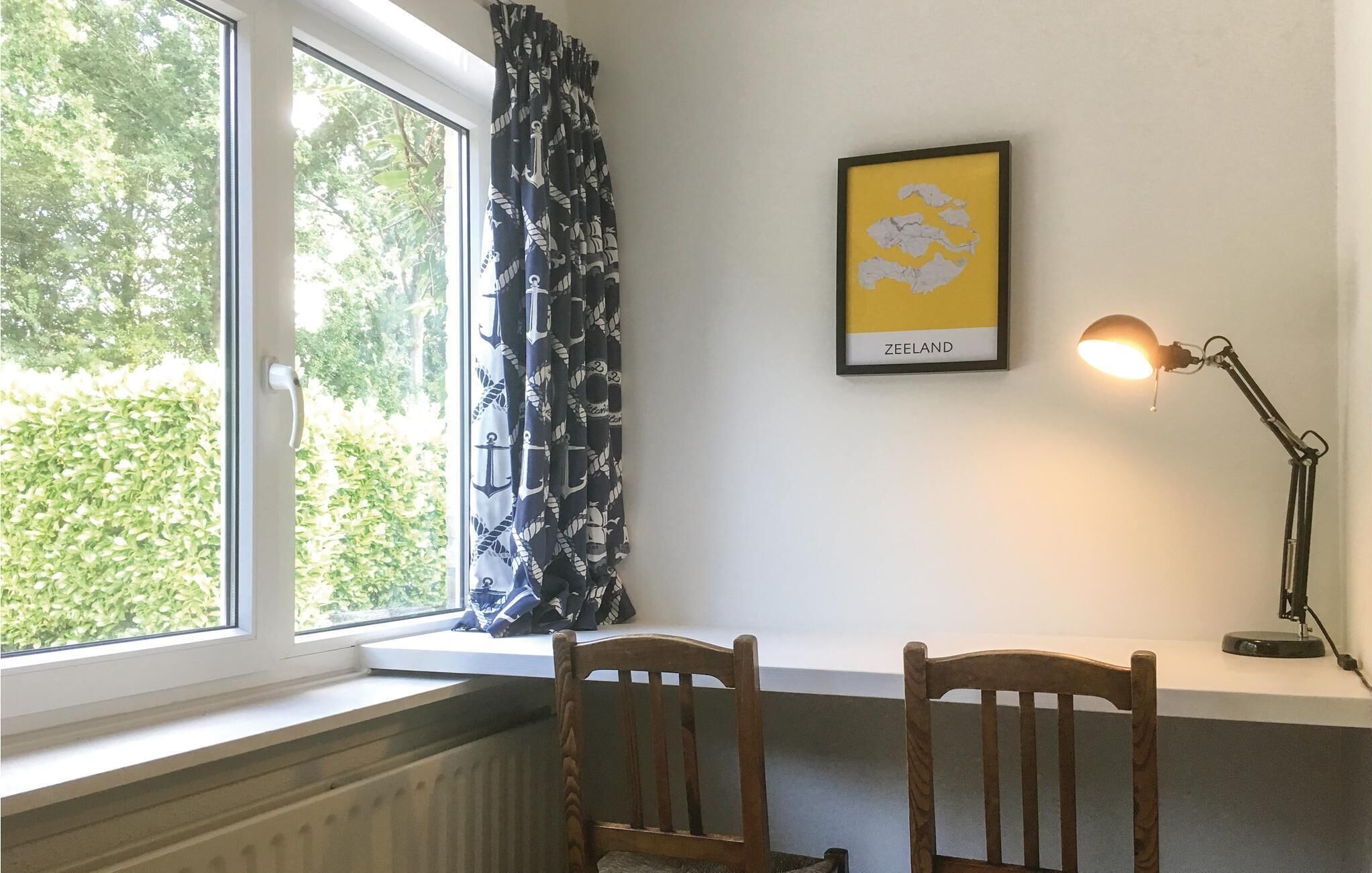 Ein Zimmer mit Fenster, einer gerahmten Karte von Seeland und einer Schreibtischlampe.