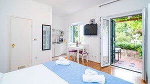 Un dormitorio con cama, escritorio, televisor y puerta corrediza de vidrio a un jardín.