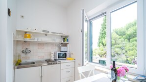Una cocina moderna con armarios blancos, un microondas y un lavamanos. Hay una ventana con vistas a árboles y un balcón.