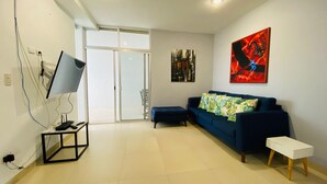 A modern living room with a blue sofa, a small white table, and a large abstract painting on the wall. - Artistic Mayan Accommodations - AMA 2C (Boulevard Turístico Bording)