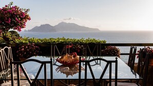 A glass table with chairs and a decorative shell centerpiece, overlooking a scenic view of the sea and mountains.
