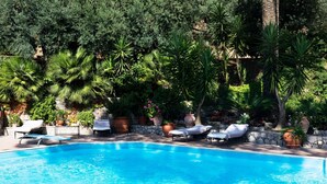 A swimming pool with lounge chairs and potted plants around it.