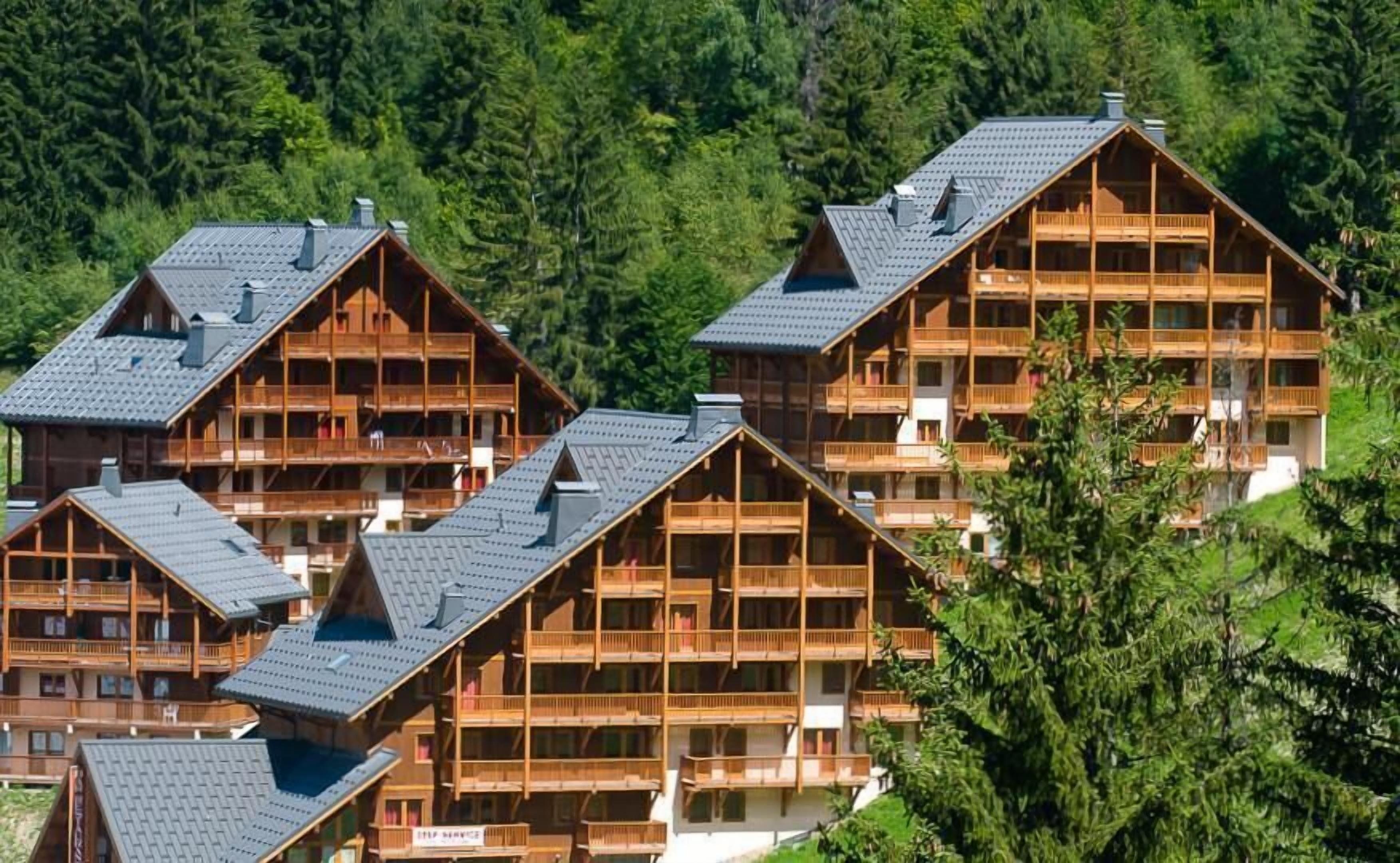 Un conjunto de cabañas de madera con varios balcones, rodeadas de un bosque denso.