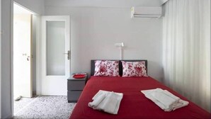Une chambre à coucher avec un lit, une table de chevet, une couvre-lit rouge et un appareil de climatisation blanc.