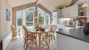 A modern kitchen with white cabinets, a dining area with wicker chairs, and large windows offering a view of the outdoors. - Pet friendly home in ålbæk with sauna (Ålbæk)