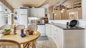 A modern kitchen with white cabinets, a dining table with wicker chairs, and a wooden ceiling. - Pet friendly home in ålbæk with sauna (Ålbæk)