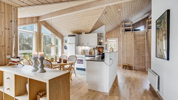 A spacious kitchen with wooden cabinets, a dining area with a table and chairs, and a large window providing natural light. - Pet friendly home in ålbæk with sauna (Ålbæk)