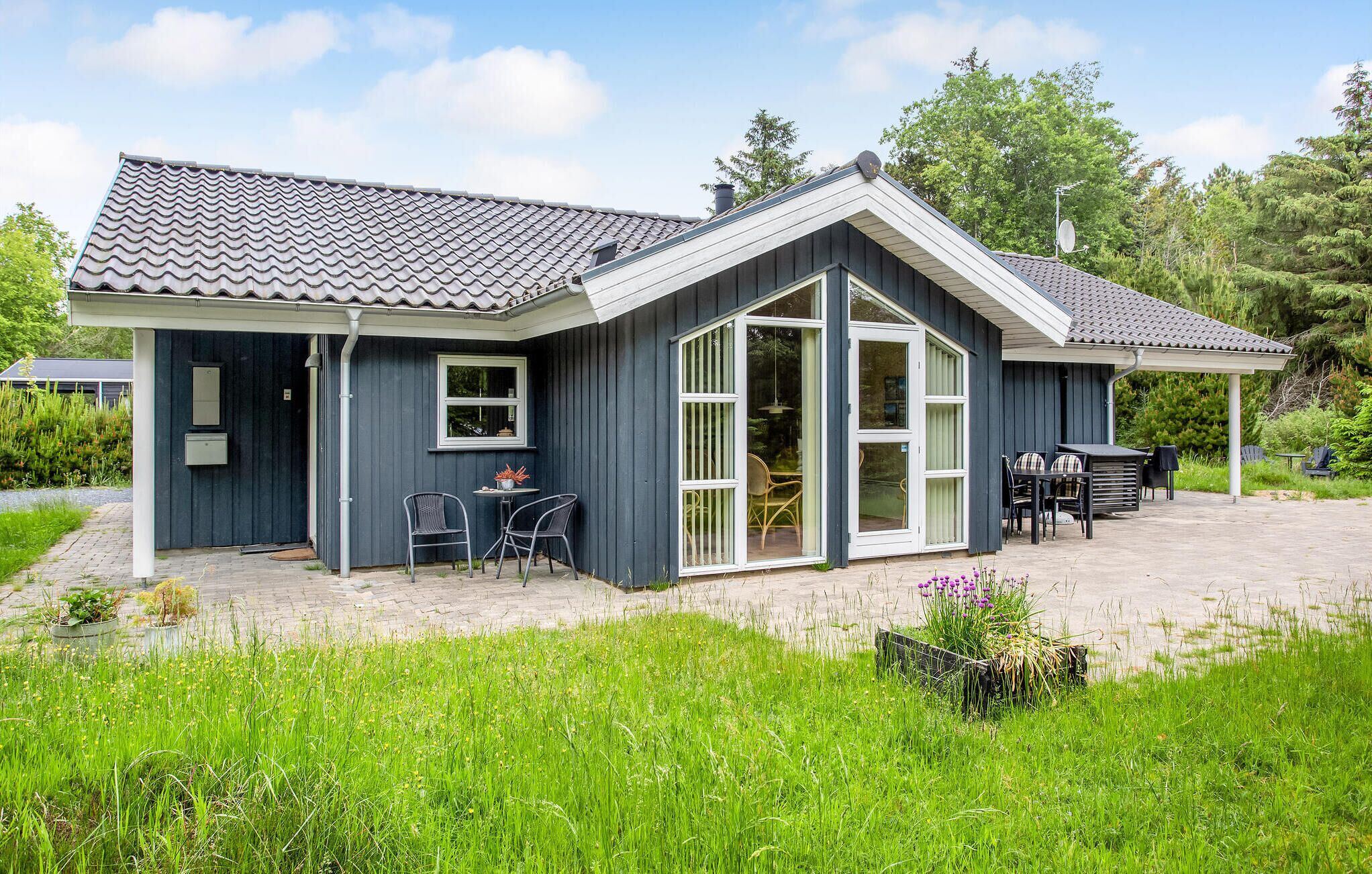 Ein modernes Haus mit überdachter Terrasse, großen Schiebetüren und einem Garten.