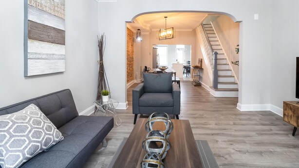 Una sala de estar moderna con un sofá gris, una mesa de centro con esferas metálicas decorativas y una escalera que sube a otro nivel.