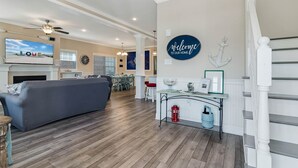 Ein geräumiges Wohnzimmer mit grauem Sofa, einem an der Wand montierten Fernseher und einem Deckenventilator.