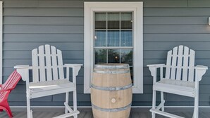Zwei Adirondack-Stühle und ein Holzbottich auf einer Veranda mit Fenster und Tür.