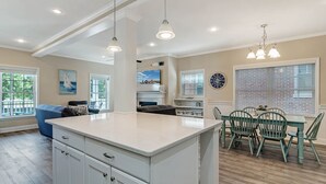 Una cocina amplia con una isla grande, piso de madera y un comedor con sillas verdes.