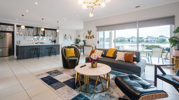 A modern living room with a sofa, coffee table, and a view of the outdoors. - Luxury Waterfront Grand Villa in Melbourne (Point Cook)