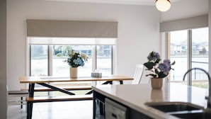 A modern kitchen with a large window, a dining table, and a sink. - Luxury Waterfront Grand Villa in Melbourne (Point Cook)