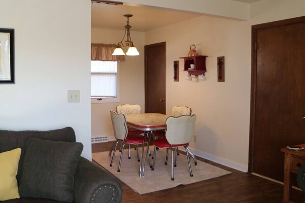 A dining area with a table and chairs, a chandelier, and a wooden door. - Peaceful Prairie Loft: BBQ + Carport (Miles City)