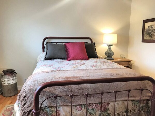 A bedroom with a metal-framed bed, floral bedding, and a bedside lamp. - Peaceful Prairie Loft: BBQ + Carport (Miles City)