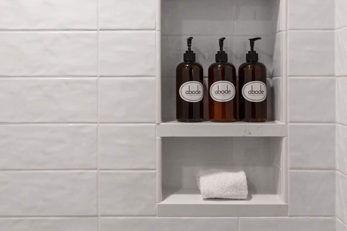 Un bagno con tre flaconi di lozione corpo Abode su uno scaffale e un asciugamano bianco sullo scaffale inferiore.