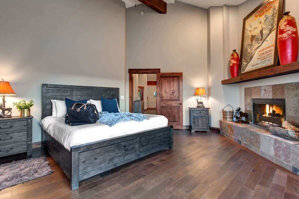A bedroom with a large bed, wooden headboard, bedside tables, a fireplace, and a door leading to another room. - Abode at Bluebird, private hot tub, steps to Main Street & trails (Park City)