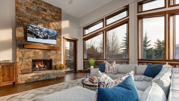 A living room with a stone fireplace, a large TV mounted on the wall, a sofa with cushions, and large windows. - Abode at Bluebird, private hot tub, steps to Main Street & trails (Park City)