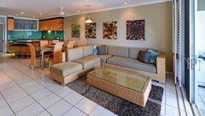Uma sala de estar moderna com sofá em formato de L, um espaço para refeições e uma cozinha ao fundo.