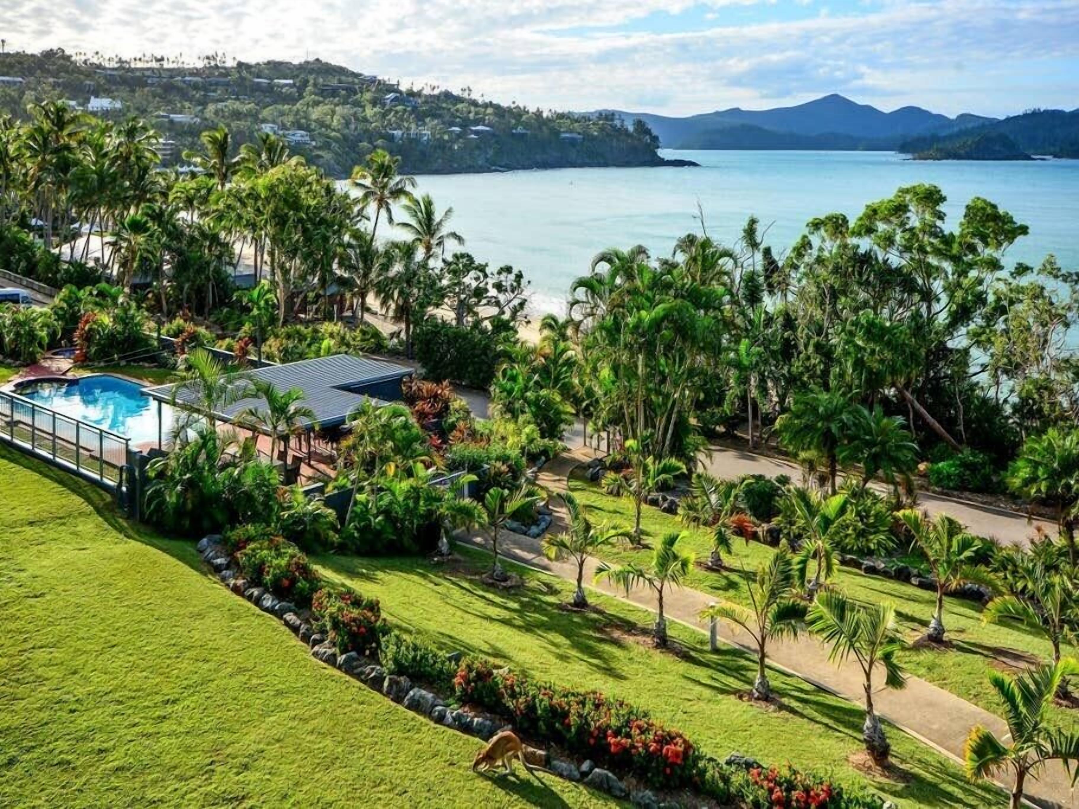 A resort with a swimming pool, lush greenery, and a view of the sea.