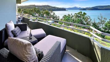 A balcony with wicker furniture, a view of a lake, and distant mountains.