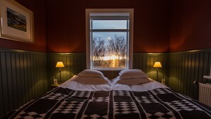 Habitació amb un llit gran, dues làmpades de nit, una finestra amb vista a arbres i un capvespre, i un quadre al mur.