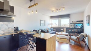 Una cocina moderna con una isla central, comedor con sillas, un sofá y una televisión en la sala de estar.
