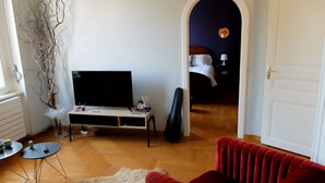 Una sala de estar con un sofá rojo, un televisor, una guitarra y una rama decorativa.