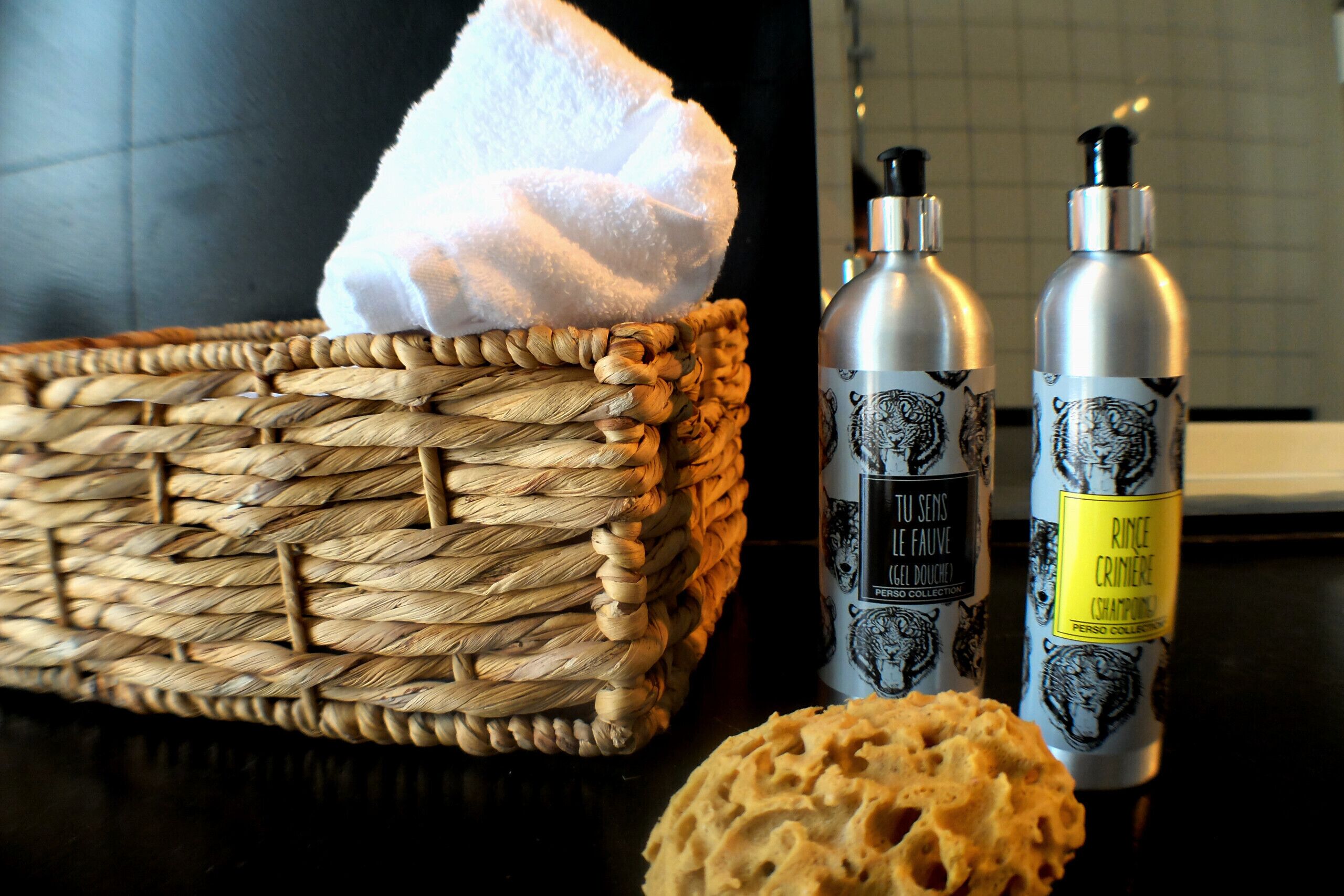Una cesta de mimbre con una toalla blanca, dos botellas de perfume y una hogaza de pan sobre una mesa.