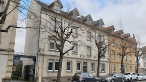 Calle con coches estacionados, árboles sin hojas y edificios históricos con numerosas ventanas y detalles arquitectónicos.