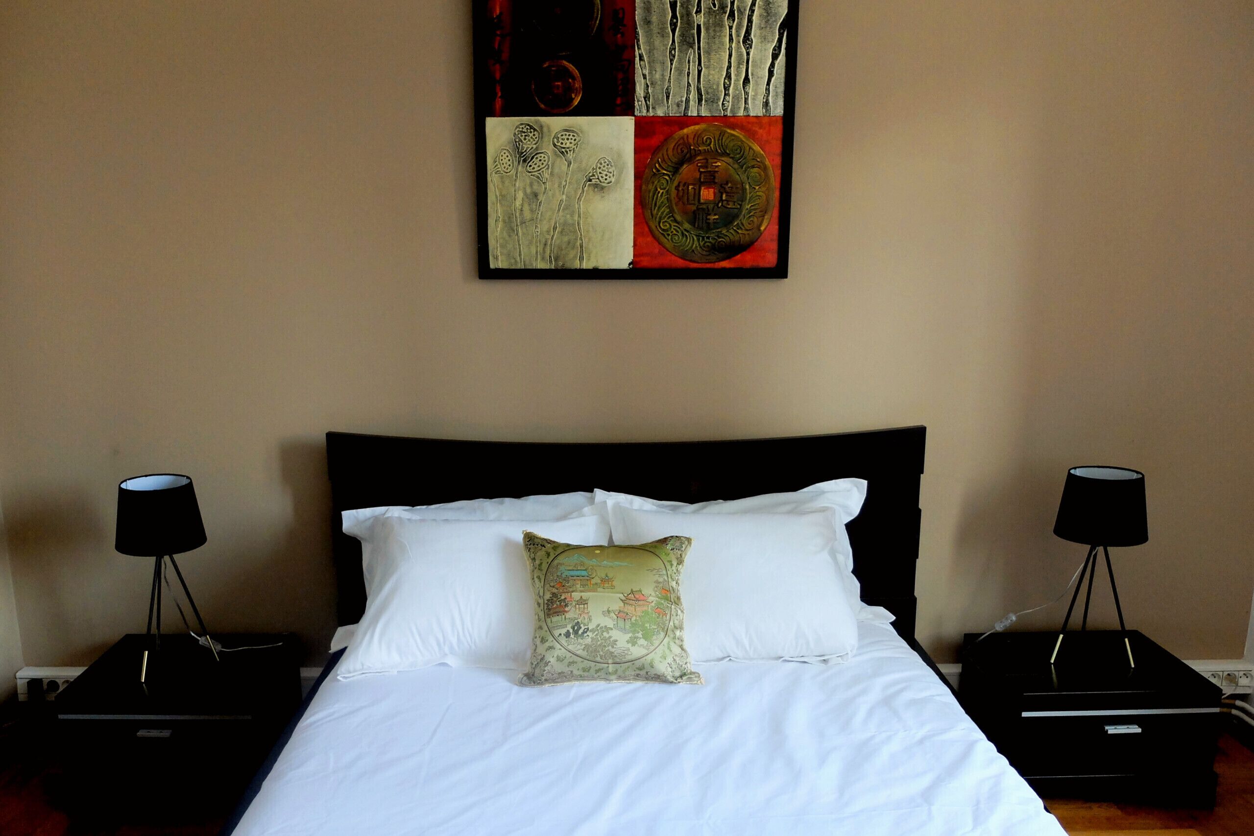 Une chambre d’hôtel comprenant un lit, deux tables de chevet, une œuvre d’art accrochée au mur et une petite table de nuit avec une lampe.