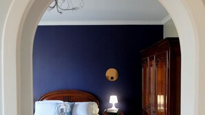 Un dormitorio con una cama, una mesita de noche con lámpara, un armario de madera y una silla rosa.