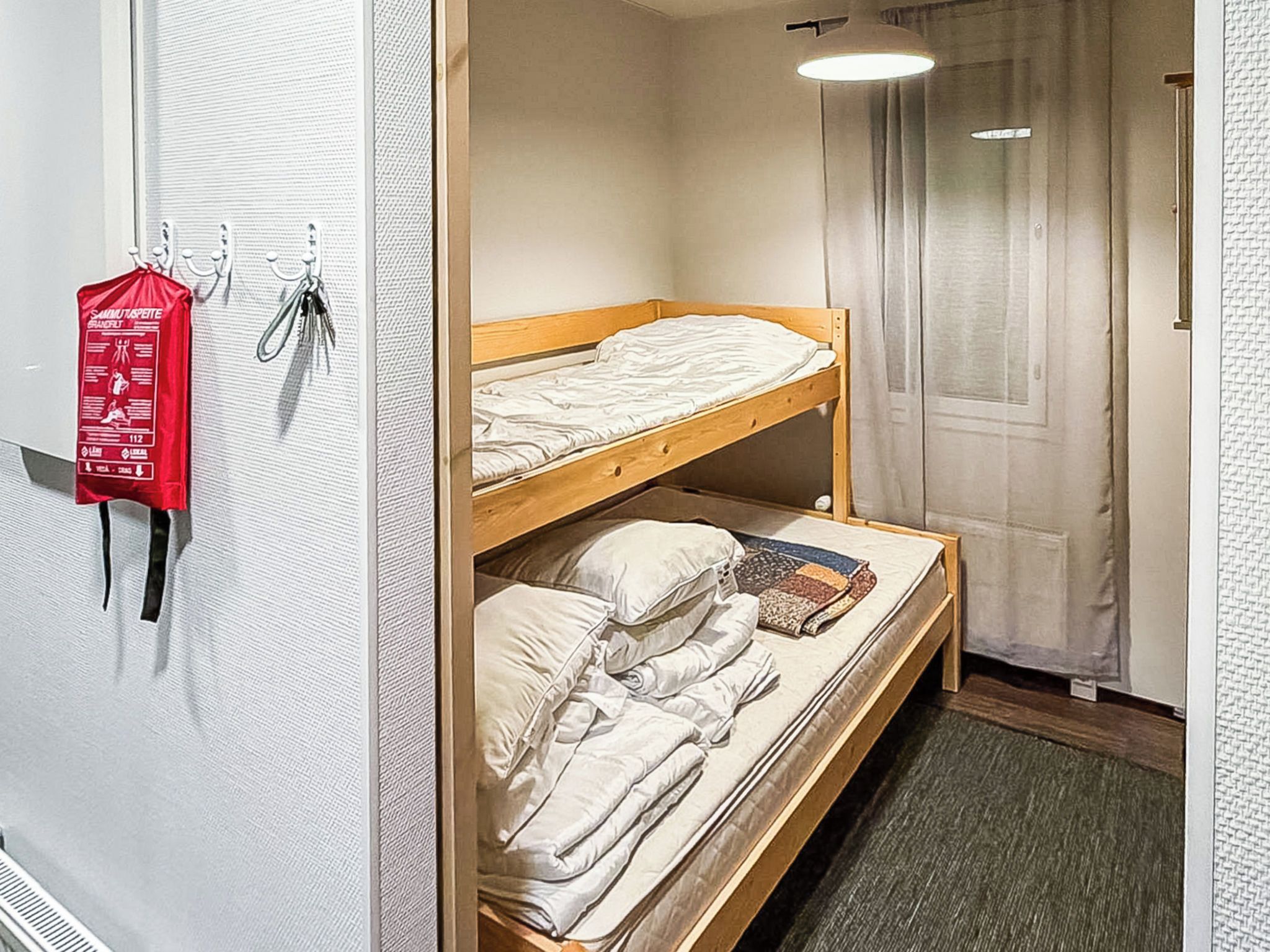 A room with a bunk bed, a red emergency exit sign, and a door with a curtain.