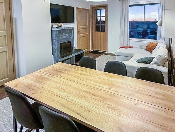 A dining area with a wooden table and chairs, a fireplace, a sofa, and a window with a view.