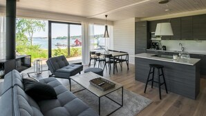 Un espacio de sala de estar moderno y abierto con cocina, ventanas amplias con vista al agua y una chimenea.