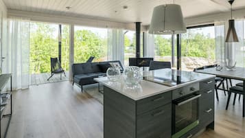 Eine moderne Küche mit einer zentralen Kochinsel, großen Fenstern und einem Essbereich mit Blick auf Grünflächen.