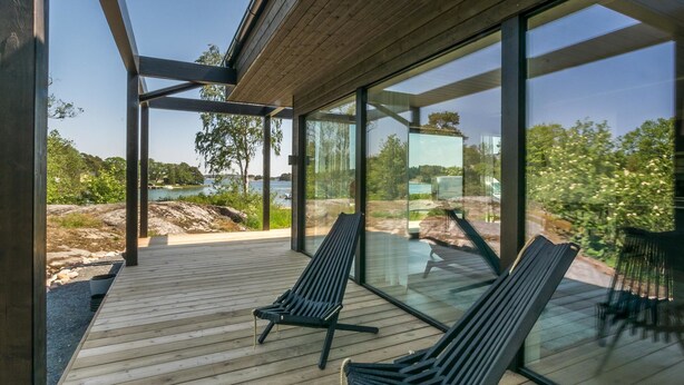 Una terraza moderna al aire libre con dos sillones reclinables negros, amplias ventanas de vidrio y vistas a un paisaje natural.