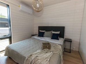 Une chambre à coucher avec un lit, une table de chevet, un panier en osier et un luminaire suspendu.