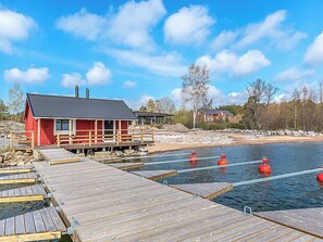 A wooden dock leading to a red building with a black roof, surrounded by a calm body of water and a forested area. - Kasnäs marina b 16 by Interhome (Kemiönsaari)
