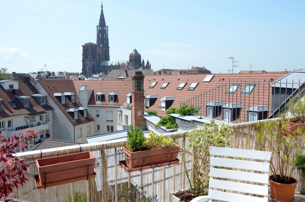 A rooftop terrace with terracotta tiles, potted plants, and a white bench.