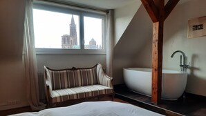 A bedroom with a large bed, a bench, a window with a view of a cathedral, and a modern sink. - emilie 145m2 ac 1 free parking 4br 2bth (Strasbourg)