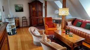 A cozy loft-style living room with a wooden floor, a large wooden cabinet, a plush armchair, a sofa with patterned cushions, a wooden coffee table, and a dining table with chairs. - emilie 145m2 ac 1 free parking 4br 2bth (Strasbourg)