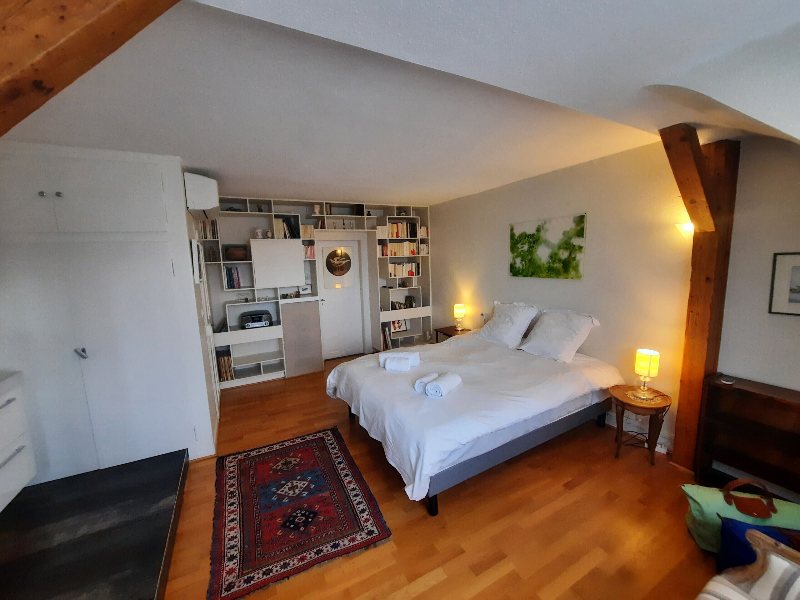 Ein Schlafzimmer mit einem Bett, Nachttischlampen, einem Bücherregal und einem kleinen Schreibtisch.