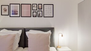 Una camera da letto con un letto, cuscini, un comodino con una lampada e una parete decorata con quadri.