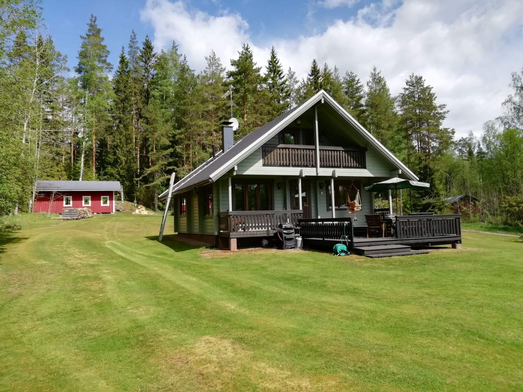 A two-story cabin with a balcony, surrounded by a well-maintained lawn and dense forest.
