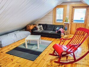 Ein gemütliches Dachzimmer mit Holzboden, einem Sofa, einem Schaukelstuhl, einem kleinen Tisch und einem Fenster mit Blick.