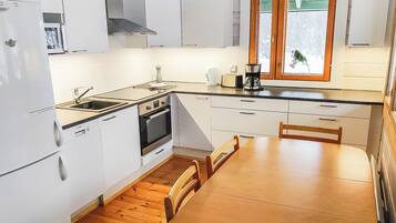 Une cuisine compacte avec des meubles blancs, une table à manger en bois et une fenêtre à vitrage dépoli.